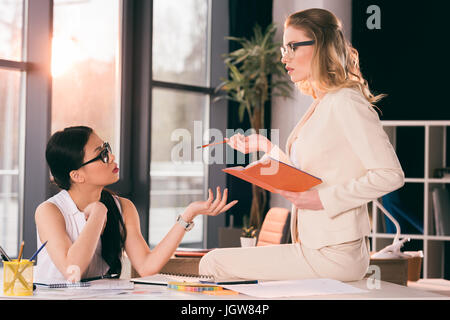 young multiethnic businesswomen in formalwear talking at modern office