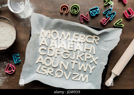 top view of dough for cookies in forms of letters with rolling pin and baking paper, cookie dough Stock Photo