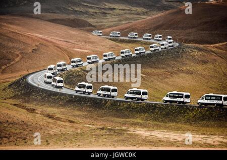 Tour bus vans on a curved road leading through a mountain landscape in Iceland. Stock Photo