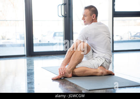 sportsman in half spinal twist pose sitting on yoga mat in gym Stock Photo