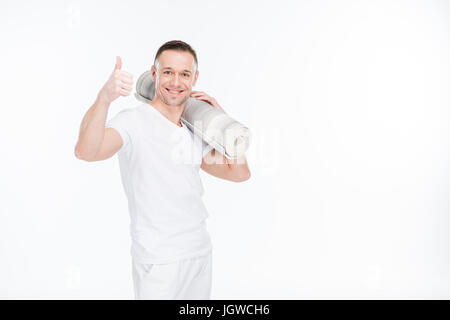 happy caucasian sportsman in white sportswear with thumb up holding yoga mat isolated on white Stock Photo