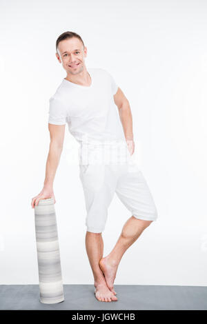 smiling caucasian sportsman in white sportswear with yoga mat standing isolated on white Stock Photo