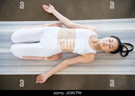above view of young asian woman doing Reclining Hero Pose (Supta Virasana) on yoga mat Stock Photo