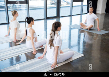 young women sitting in lotus pose with instructor indoors Stock Photo