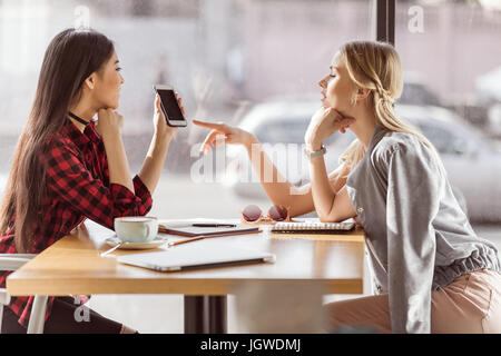 Side view of young women talking while having business lunch meeting in cafe Stock Photo