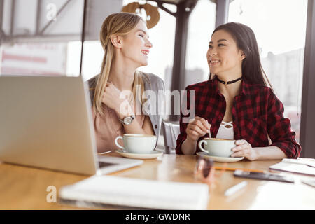 Beautiful young women drinking coffee and using laptop in cafe at lunch meeting Stock Photo