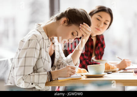 pensive girls sitting at coffee break and writing at notebooks, business lunch Stock Photo