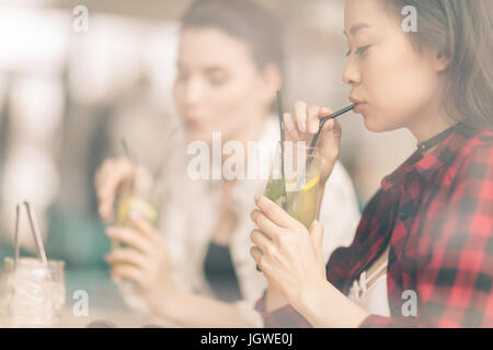 young girls drinking cocktails together while sitting at table in cafe, having lunch Stock Photo