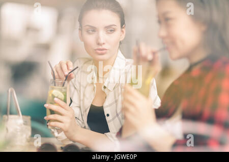 young girls drinking cocktails together while sitting at table in cafe, having lunch Stock Photo