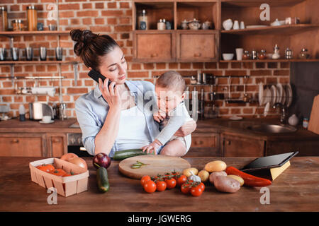 Portrait of mother with son talking on smartphone and preparing dinner in the kitchen Stock Photo
