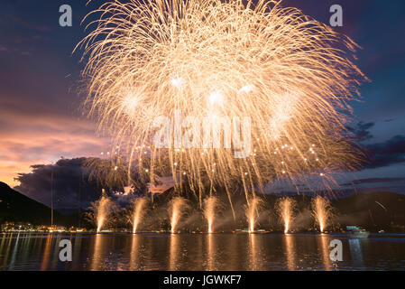 Fireworks on the Lugano Lake in a summer evening with cloudy sky at the sunset in the background Stock Photo