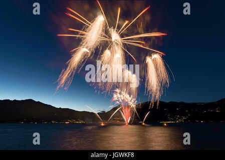 Fireworks on the lakefront of Luino over the Maggiore Lake in a summer evening with blue sky and mountains in the background