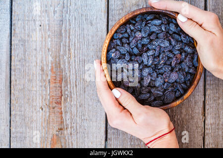 Black raisins in a wooden bowl. Healthy light snack, dried fruit, top view.