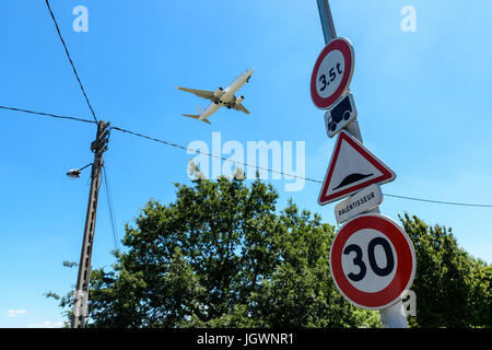 An airliner in landing approach flying above a residential area with roadsigns in the foreground. Stock Photo