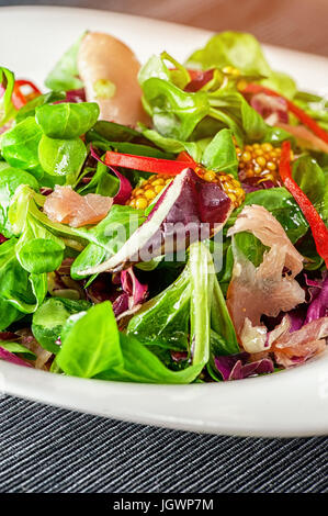 a dish of different types of colorful lettuce, arugula, prosciutto, olive oil and Dijon mustard in a white glass container.The vertical frame. Stock Photo