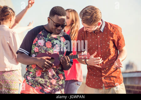 Young man playing ukulele at roof party in London, UK Stock Photo