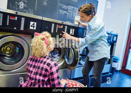 Laundrette business owner showing woman washing machine control panel Stock Photo