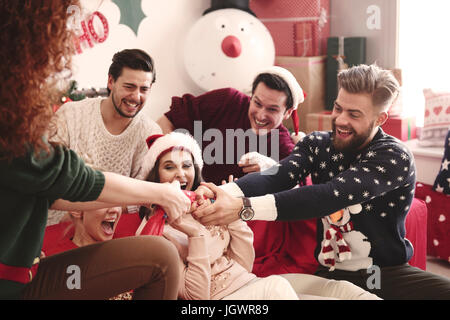 Young adult friends pulling christmas crackers on sofa at christmas party Stock Photo