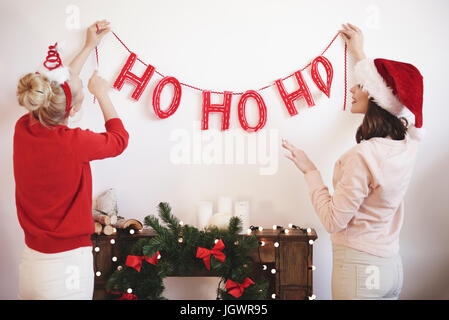 Rear view of two young women putting up christmas decorations on wall Stock Photo
