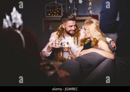Man and woman at party, sitting on sofa, holding drinks, making a toast Stock Photo