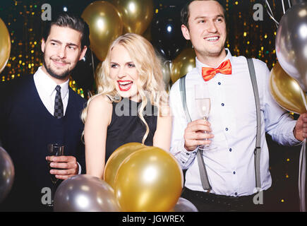 Portrait of three people at party, surrounded by balloons, holding champagne glasses Stock Photo