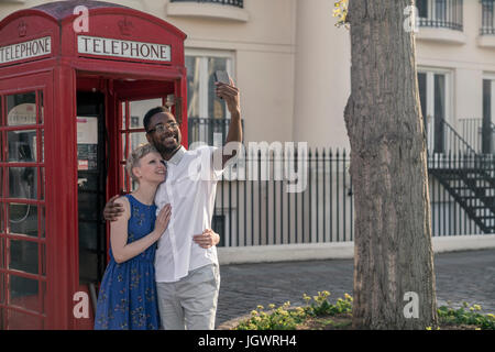 Young couple standing beside red telephone box, looking up, smiling Stock Photo