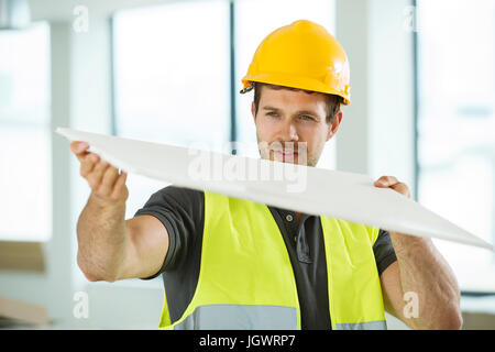 Man wearing hi vis vest, standing in newly constructed space, looking at construction material Stock Photo