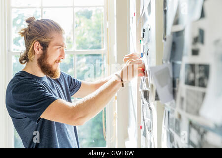 Young male designer pinning mood board ideas to wall in creative studio Stock Photo