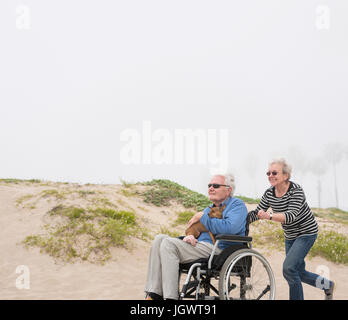 Senior woman pushing husband in wheelchair on dunes, Playa del Ray, California, USA Stock Photo