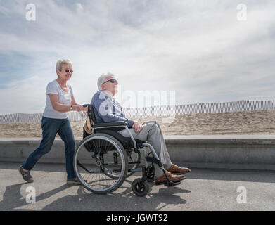 Senior woman pushing husband in wheelchair at beach, Santa Monica, California, USA Stock Photo