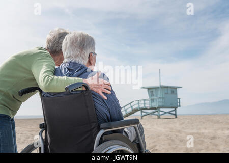 Senior man in wheelchair with wife looking out from beach, Santa Monica, California, USA Stock Photo