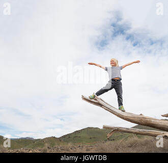 Boy balancing on end of tree trunk, sky in background Stock Photo