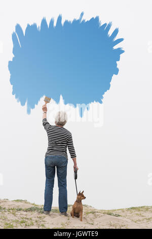 Senior woman with dog on lead painting blue sky in air Stock Photo