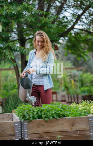 Young woman watering plants in trough, with watering can Stock Photo
