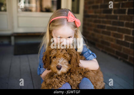 Portrait of girl kissing red haired puppy on front porch