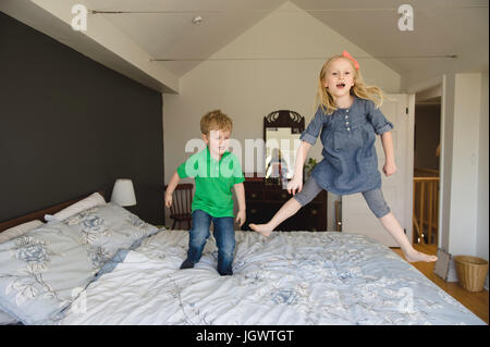 Girl and brother jumping on bed together Stock Photo