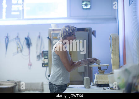 Senior woman in pottery workshop, weighing clay for pottery project Stock Photo