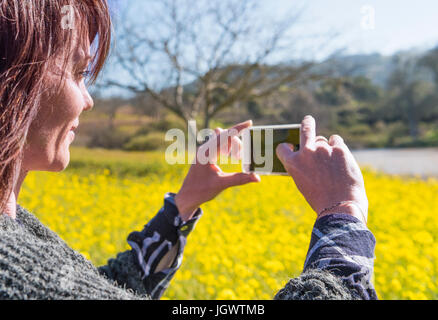 Mature woman outdoors, in rural setting, taking picture using smartphone Stock Photo