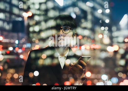 Businesswoman using mobile phone behind glass reflection of buildings, Milan, Italy Stock Photo