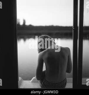 Boy sitting on edge of barge, rear view Stock Photo