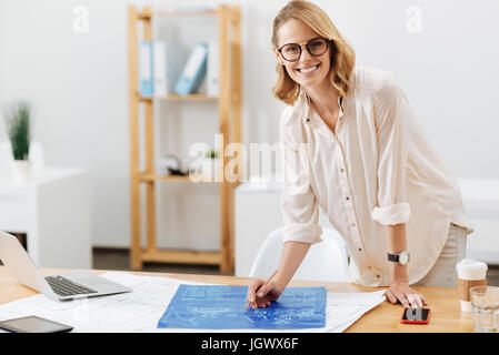 Design of your home in my hands. Delighted smart skilled architect working on the project and preparing the draft while using digital gadgets and smil Stock Photo