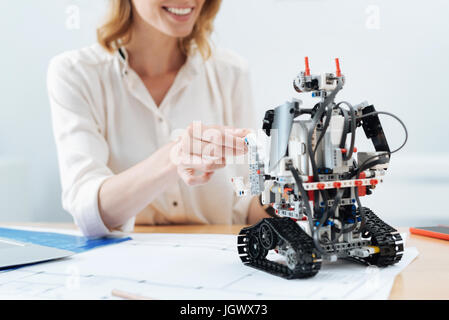 Making friends with robot. Delighted positive glad woman smiling and working in the office while looking at the electronic robot and making friends wi Stock Photo