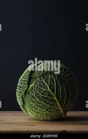 A whole green cabbage on a raw wood planked table, against a black chalkboard background.  Moody lighting. Stock Photo