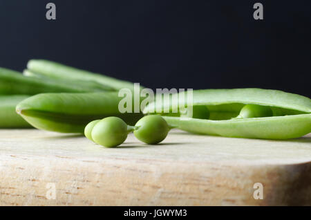 Close up (macro) of three peas with stalks intact on wooden chopping board. The opened pod from which they were extracted lies behind, and unopened po Stock Photo