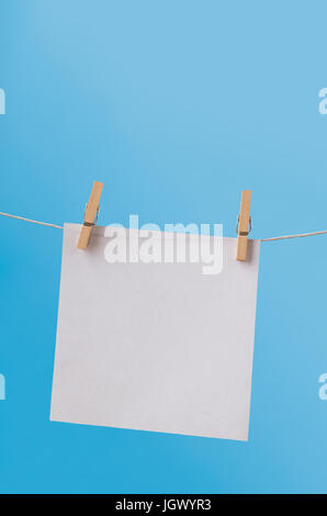 One, single sheet of white, square paper, hanging from a clothes line on wooden pegs against a clear blue sky.  Left blank for copy space. Stock Photo