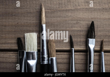 Overhead photograph of a variety of artist's paintbrushes arranged on old, faded wood. Stock Photo