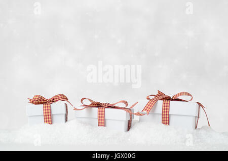 Eye level shot of three white Christmas gift boxes with lids, in a row and bow tied with gingham checked ribbons, nestling in artificial snow with spa Stock Photo