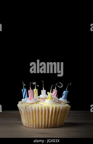 A birthday cupcake in a  plain paper case with seven striped candles that have burned down and been blown out.  Placed  on a wooden table with black b Stock Photo