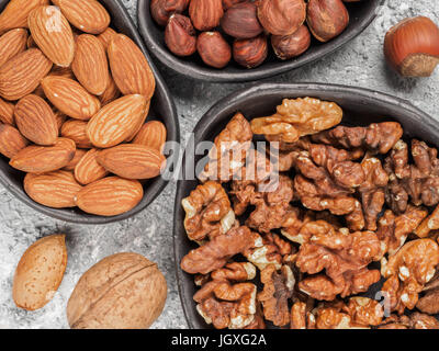 Walnuts, almonds and hazelnuts in trendy plates on gray cement background. Top view or flat lay. Stock Photo