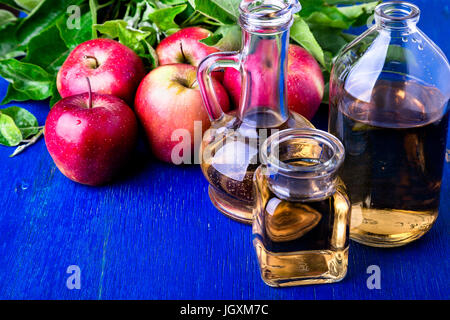 Apple cider vinegar. Three glass bottle on blue background. Red apples Stock Photo
